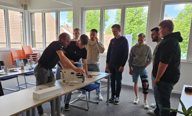 Gruppe beobachtet Demonstration an technischem Gerät im Raum.